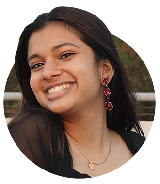A smiling headshot of Layla Zaidi wearing long red earrings and a gold necklace.  